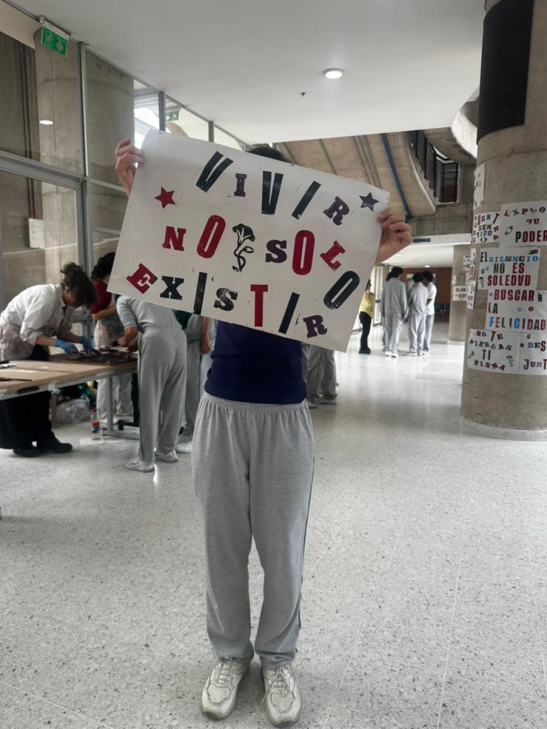 Estudiante del Colegio Próspero Pinzón sostiene un cartel impreso manualmente con la frase "Vivir no solo existir" en letras de madera.